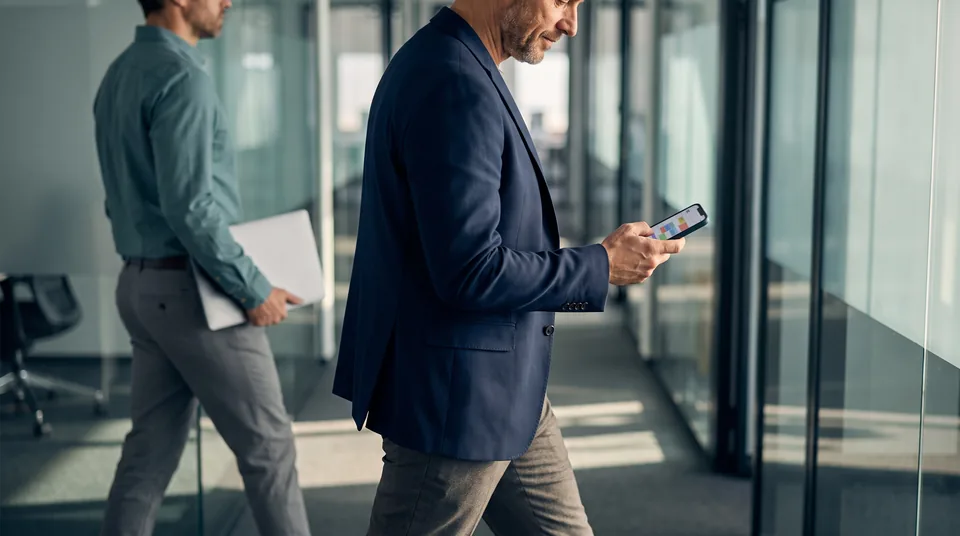 Executive between back-to-back meetings checking a calendar on a phone in an office corridor